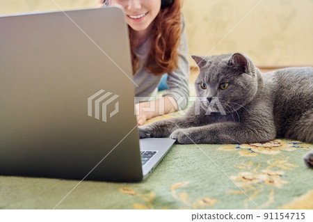 Preteen girl in headphones and gray british cat looking at laptop together 91154715