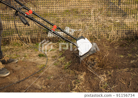 Male farmer plows the land with a cultivator. Agricultural machinery for tillage in the garden, combine harvester. Male farmer plows the land with a cultivator. Agricultural machinery for tillage in the garden, combine harvester. 91156734