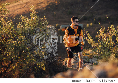 Male Hiker with Backpack and Digital Camera Walking on the Hill During Sunset, Traveler Man in Solo Trip Male Hiker with Backpack and Digital Camera Walking on the Hill During Sunset, Traveler Man in Solo Trip 91158067