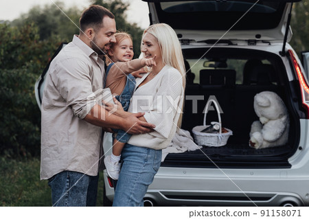Young Parents with Their Toddler Daughter Hugging in front of the SUV Car, Family Enjoying Road Trip Weekend 91158071