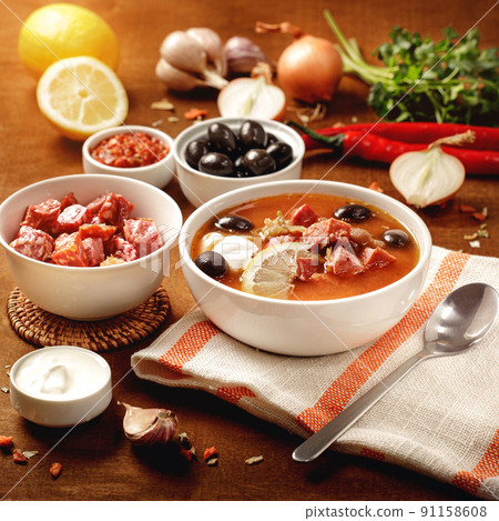 Meat Solyanka soup on with ingridients, sausage, olive,lemon, parsley, garlic, yogurt. Ukrainian food. Wooden background. 91158608