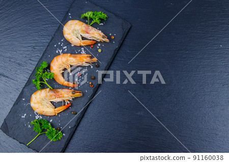 Big raw red prawns with parsley, salt and pepper on a slate board on black background. Top view, copy space 91160038