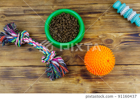 Dog toys and feed for dogs in green plastic bowl on wooden background. Top view. Dog care concept Dog toys and feed for dogs in green plastic bowl on wooden background. Top view. Dog care concept 91160437