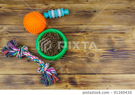 Dog toys and feed for dogs in green plastic bowl on wooden background. Dog care concept 91160438