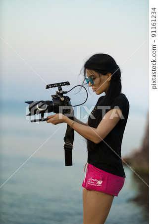 Female videographer filming a seascape with a professional movie camera Female videographer filming a seascape with a professional movie camera 91161234