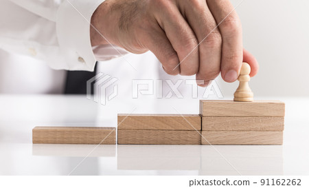 Businessman placing a chess piece on wooden steps Businessman placing a chess piece on wooden steps 91162262