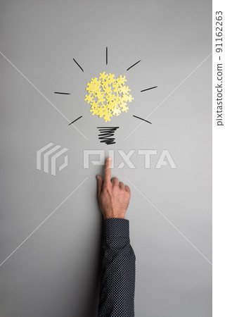 Hand of a businessman pointing on a light bulb made of yellow puzzle pieces Hand of a businessman pointing on a light bulb made of yellow puzzle pieces 91162263