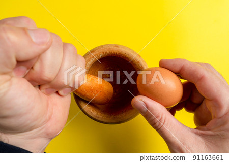 Man's hand with a wooden kitchen mortar with an egg in the other hand prepared to make a sauce Man's hand with a wooden kitchen mortar with an egg in the other hand prepared to make a sauce 91163661