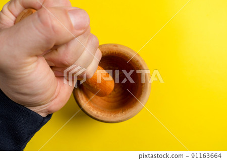 Man's hand with a wooden kitchen mortar prepared to make a sauce. 91163664