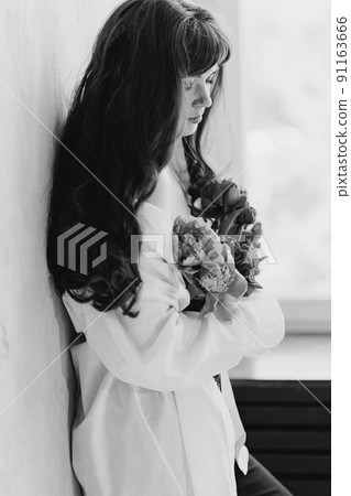 a beautiful young brunette woman in a white shirt with a bouquet of peonies. 91163666