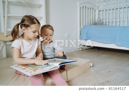 cute little boy and a boy reading book in child room. cute little boy and a boy reading book in child room. 91164517