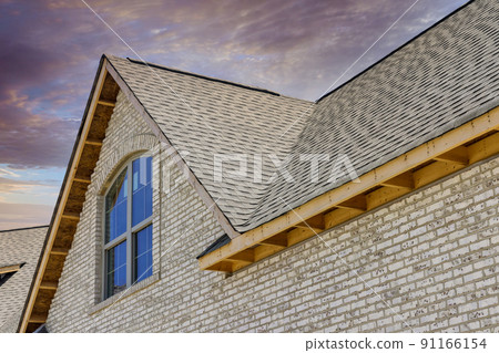A new house is being constructed with asphalt shingles and waterproofing for the corner roof shingles A new house is being constructed with asphalt shingles and waterproofing for the corner roof shingles 91166154