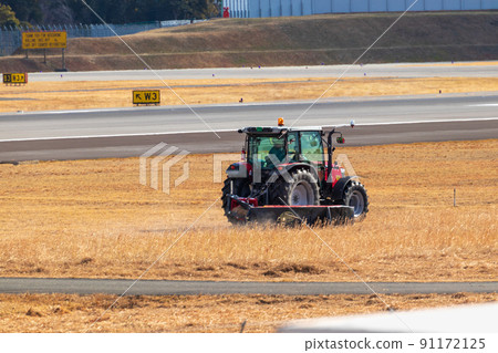 A tractor working on the grass next to the runway 91172125