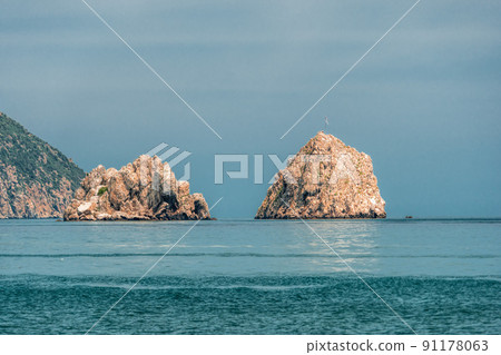 GURZUF, CRIMEA - View from a beach in Gurzuf on the famous rocks Adalary (Two Twin-Cliffs) with an edge of mountain Au-Dag in early spring morning at the South coast of Crimean Peninsula. Copy space. GURZUF, CRIMEA - View from a beach in Gurzuf on the famous rocks Adalary (Two Twin-Cliffs) with an edge of mountain Au-Dag in early spring morning at the South coast of Crimean Peninsula. Copy space. 91178063