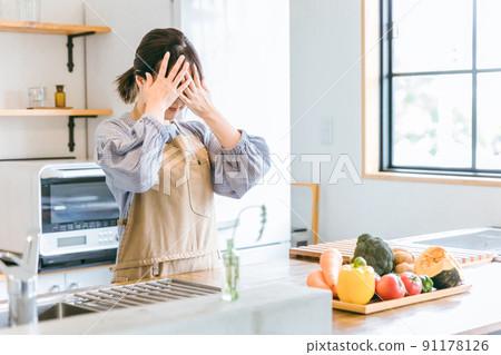 A woman in an apron who is not good at cooking in the kitchen (worried / troubled) 91178126