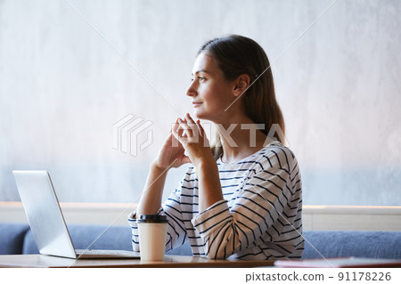 Introspective purposeful young lady sitting at table in modern cafe and thinking of new internet project 91178226