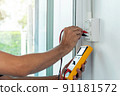 Electrician using a digital meter to measure the voltage at a wall socket. 91181572