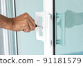 Man's hand opening a glass door with a key. 91181579