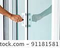 Man's hand opening a glass door with a key. 91181581