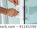 Man's hand opening a glass door with a key. 91181598