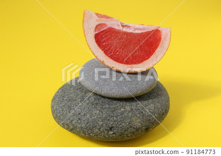 a ballans tower of grey stones and grapefruit orange fruit on a white yellow background with room for text. Benefits of Energy Health Importance Vitamin 91184773
