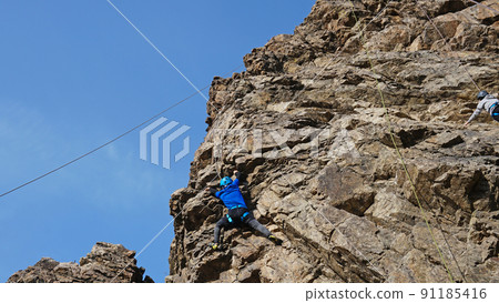 A guy high up on a cliff is trying to grab a ledge 91185416
