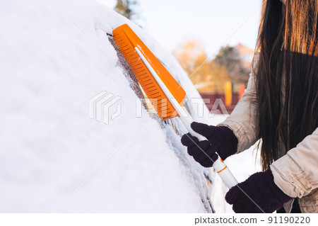 Woman cleans car with a brush from snow after a blizzard 91190220