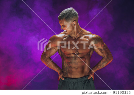 A handsome confident athletic man with bare mscular torso posing on a dark background filled with smoke. Male beauty concept. Fitness, bodybuilding A handsome confident athletic man with bare mscular torso posing on a dark background filled with smoke. Male beauty concept. Fitness, bodybuilding 91190335