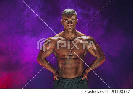 A handsome confident athletic man with bare mscular torso posing on a dark background filled with smoke. Male beauty concept. Fitness, bodybuilding A handsome confident athletic man with bare mscular torso posing on a dark background filled with smoke. Male beauty concept. Fitness, bodybuilding 91190337