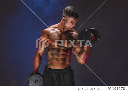 Brutal sweaty strong young man athlete with naked upper body standing doing workout with dumbbels and showing strong pumped up biceps over smoky background. Sport men body concept Brutal sweaty strong young man athlete with naked upper body standing doing workout with dumbbels and showing strong pumped up biceps over smoky background. Sport men body concept 91191678