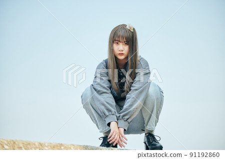 Gen Z woman sitting looking at the camera against the blue sky 91192860
