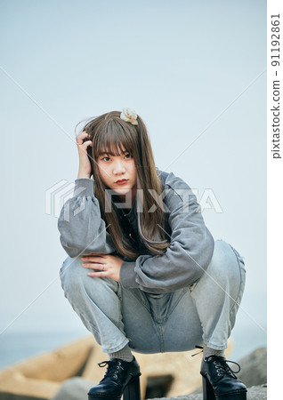 Gen Z woman sitting looking at the camera against the blue sky 91192861
