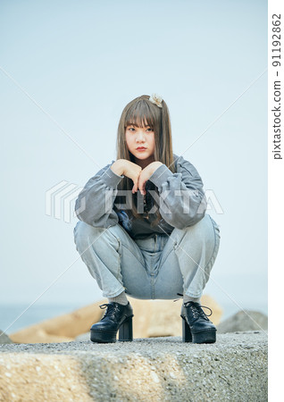 Gen Z woman sitting looking at the camera against the blue sky 91192862