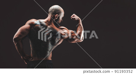 BAck view of a muscular man with tattoo on back against of black background. Isolated BAck view of a muscular man with tattoo on back against of black background. Isolated 91193352