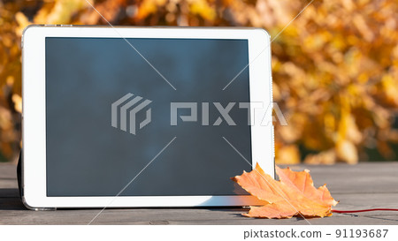 Tablet with a blank screen on the table against the backdrop of an autumn park. Template for design or advertising 91193687