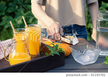 Girl cooking summer orange cocktail with mint and ice cubes outdoors, selective focus Girl cooking summer orange cocktail with mint and ice cubes outdoors, selective focus 91193702