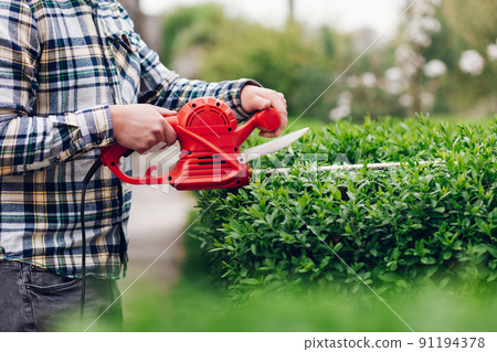 Man mows shrubs with electric trimmer for bushes. 91194378