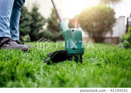 Man cuts grass with electric trimmer.. 91194501