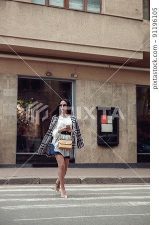 Beautiful stylish businesswoman in sunglasses crossing the street road and testing on phone. Beautiful stylish businesswoman in sunglasses crossing the street road and testing on phone. 91196105