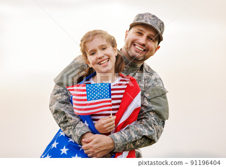 Happy girl daughter with american flag hugging father came back from US army Happy girl daughter with american flag hugging father came back from US army 91196404