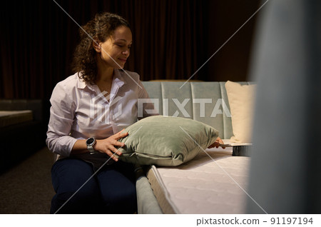 A warehouse worker, retailer, clerk using brush, cleans the dust from velour cushion before preparing it for display in the furniture store showroom 91197194