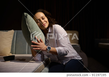 Beautiful multi ethnic woman gently hugging a velour soft pillow gently leaning against it while cleaning an orthopedic mattress in a home interior 91197195