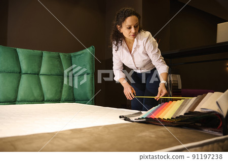 Inspired freelancer woman, Interior designer selecting a new upholstery for soft bed, measures the dimensions of upholstered furniture in the bedroom Inspired freelancer woman, Interior designer selecting a new upholstery for soft bed, measures the dimensions of upholstered furniture in the bedroom 91197238