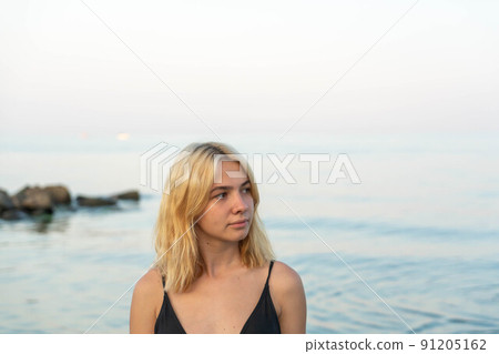 Young blonde woman on a rocky seashore after sunset. Odessa. Ukraine. 91205162