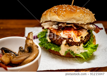 Homemade beef burger with lettuce, tomato, mushrooms and cheese on a wooden board with black background. Chopped view. Copy text. Fastfood concept. 91215847