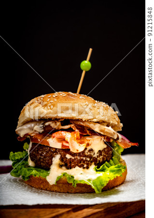 Homemade beef burger with lettuce, tomato, mushrooms and cheese on a wooden board with black background. Normal view. Copy text. Fastfood concept. Homemade beef burger with lettuce, tomato, mushrooms and cheese on a wooden board with black background. Normal view. Copy text. Fastfood concept. 91215848