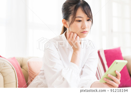 Thinking of a woman watching a smartphone in a room 91218194