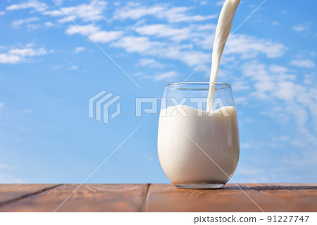 milk pouring into glass on table with blue sky and clouds 91227747