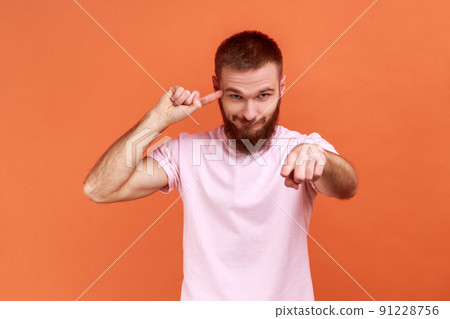 Portrait of bearded man showing stupid gesture and pointing to camera, blaming for insane plan, crazy idea, dumb suggestion, wearing pink T-shirt. Indoor studio shot isolated on orange background. Portrait of bearded man showing stupid gesture and pointing to camera, blaming for insane plan, crazy idea, dumb suggestion, wearing pink T-shirt. Indoor studio shot isolated on orange background. 91228756