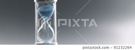 Closeup of hourglass with blue sand on gray background 91232264